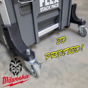Könnte beinhalten: Eine graue Milwaukee Werkzeugbox mit dem Text "FLEX STACK PACK" auf der Seite. Die Werkzeugbox hat vier schwarze Räder mit grauen Gummireifen. Der Text "3D PRINTED!" ist in Gelb auf dem Boden vor der Werkzeugbox gedruckt.