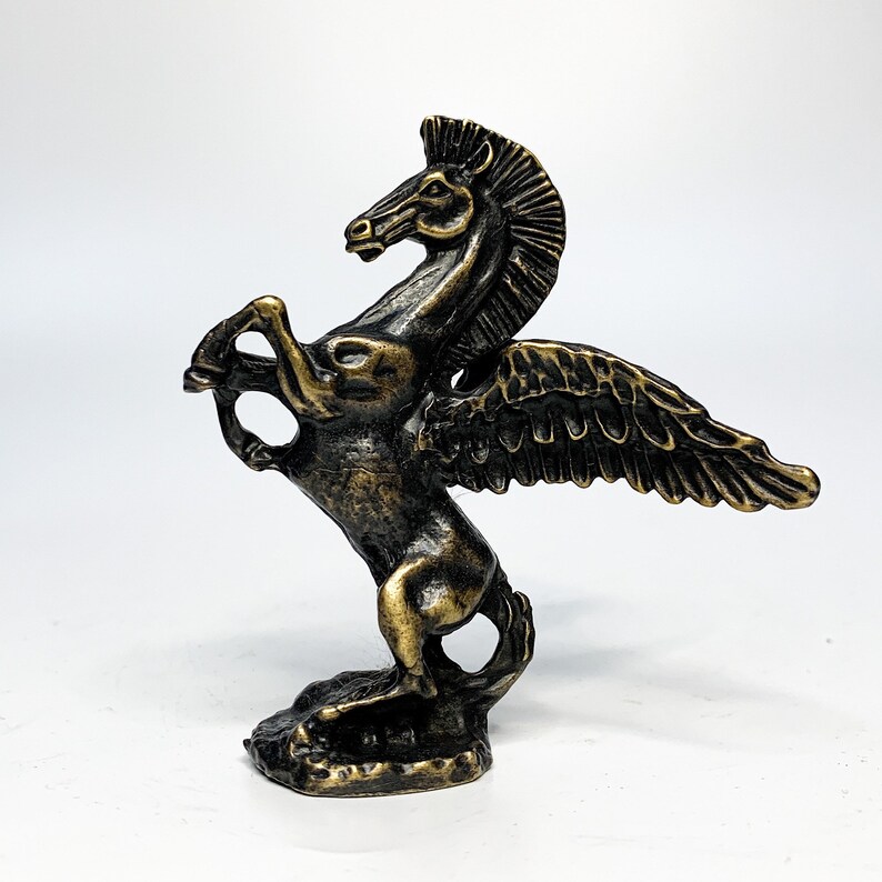 May include: A bronze winged horse statue with a detailed design. The horse is standing on its hind legs with its wings spread out. The statue is a dark bronze colour with a gold finish.