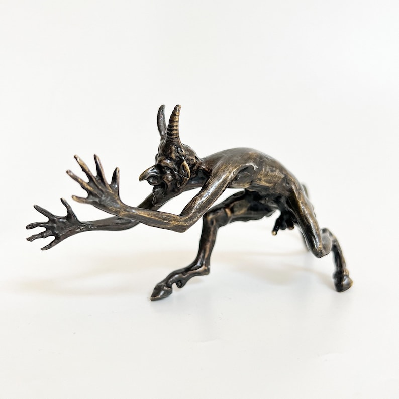 May include: A bronze sculpture of a horned creature with a human-like body and goat-like legs. The creature is in a crouched position with its arms outstretched.