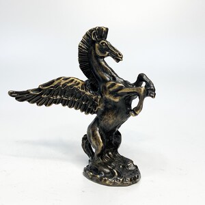 May include: A bronze sculpture of a winged horse, or pegasus, with its wings spread out and its head turned to the side. The horse is standing on a base.