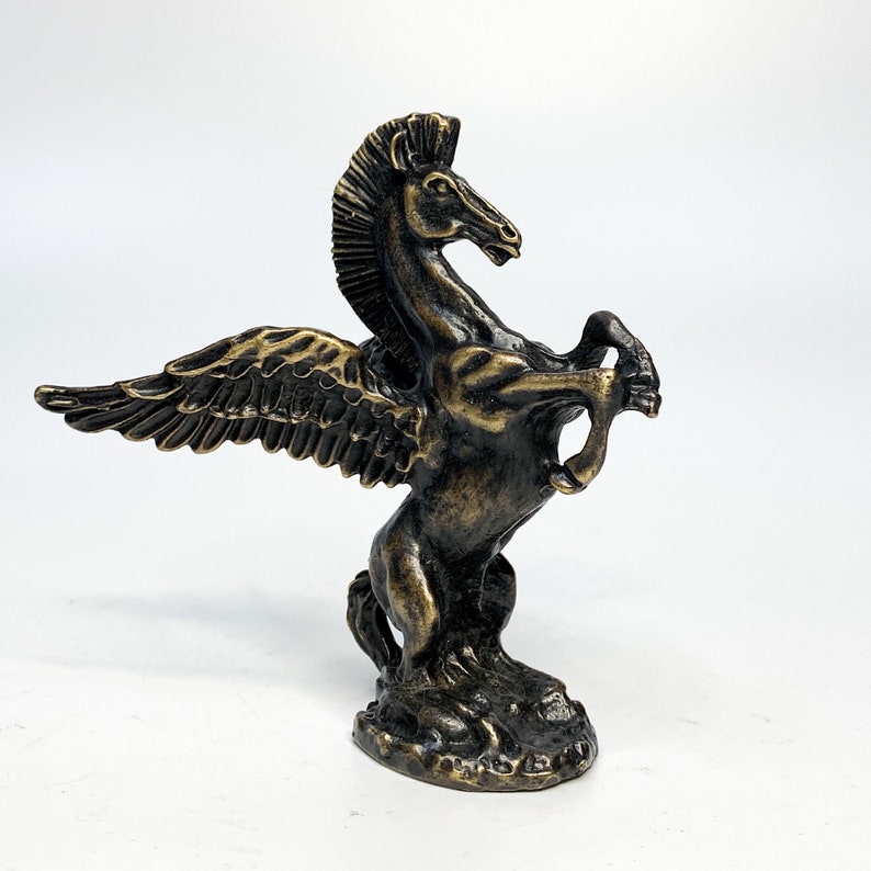 May include: A bronze sculpture of a winged horse, or pegasus, with its wings spread out and its head turned to the side. The horse is standing on a base.