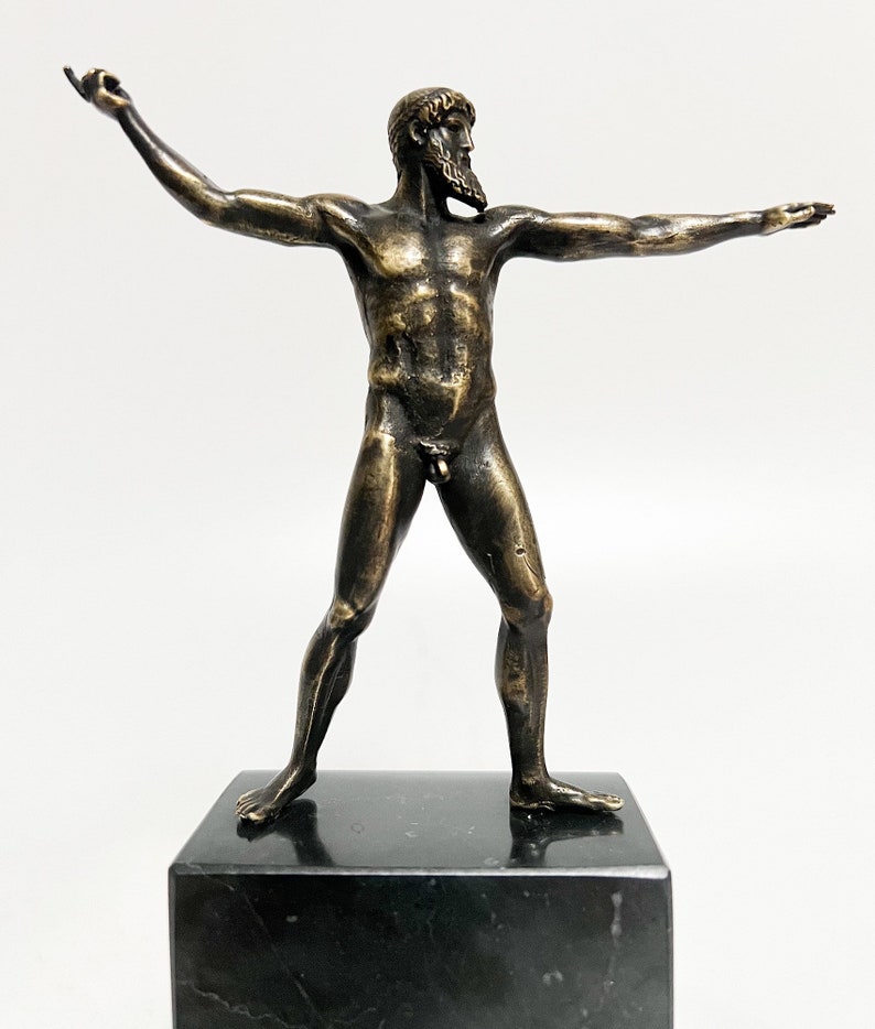 May include: A bronze sculpture of a nude male figure standing with arms outstretched. The sculpture is on a black marble base.