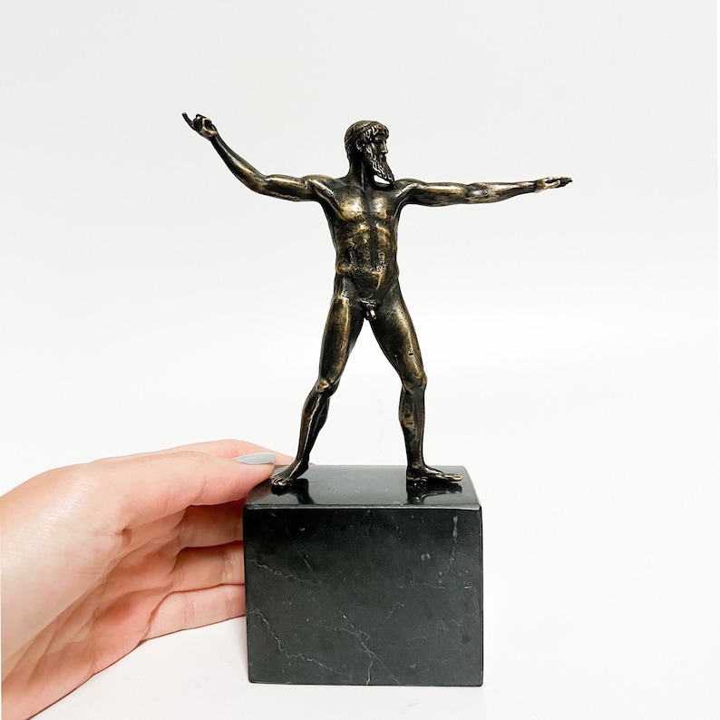 May include: Bronze sculpture of a nude male figure standing on a black marble base. The figure has a beard and is posed with arms outstretched.