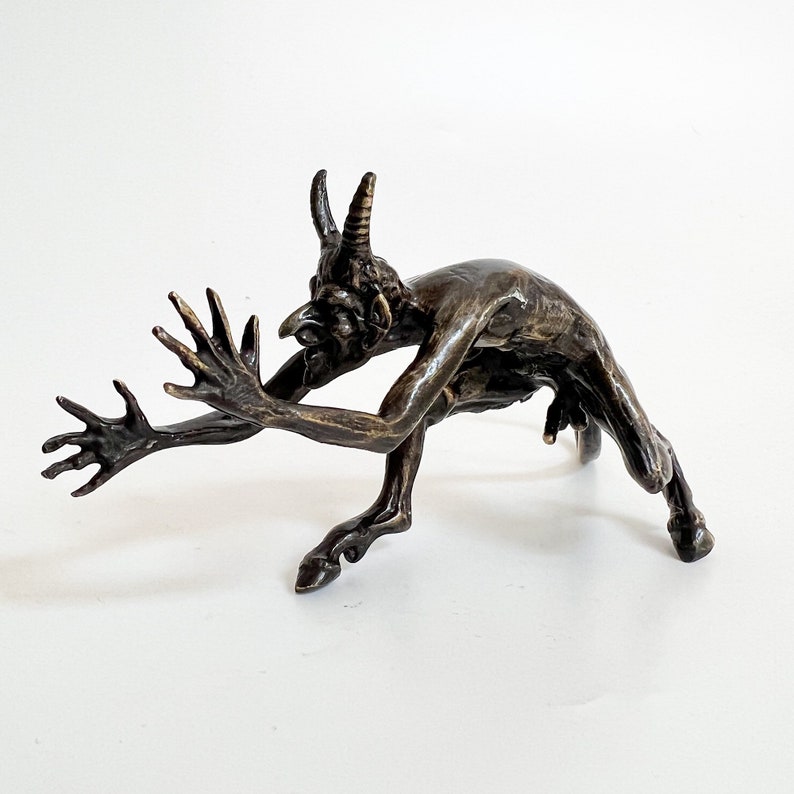 May include: A bronze sculpture of a horned figure with a hunched back and outstretched arms. The figure appears to be running or leaping forward.