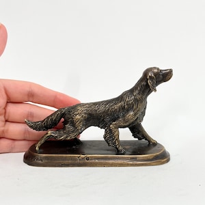 May include: A bronze sculpture of a dog, possibly a setter, in a running pose. The dog is depicted with a long, flowing tail and a determined expression. The sculpture is mounted on a rectangular base.