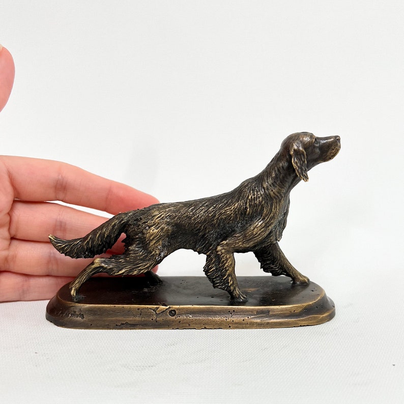 May include: A bronze sculpture of a dog, possibly a setter, in a running pose. The dog is depicted with a long, flowing tail and a determined expression. The sculpture is mounted on a rectangular base.