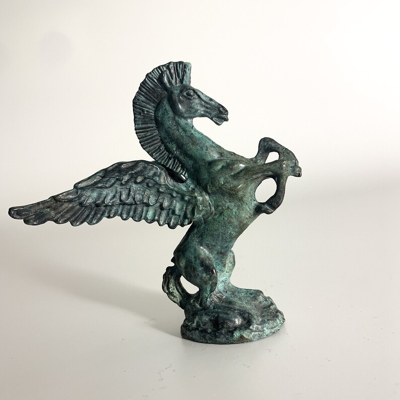 May include: A green bronze sculpture of a winged horse, or pegasus, with its wings spread out. The horse is standing on its hind legs and has its head turned to the side.