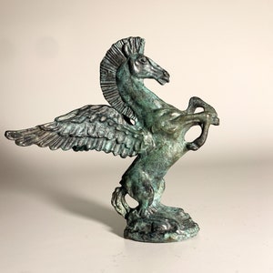 May include: A green bronze sculpture of a winged horse, or Pegasus, with its wings spread out. The horse is standing on its hind legs and has its head turned to the side.