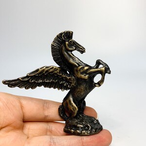 May include: A bronze winged horse statue with a detailed design. The horse is standing on its hind legs with its wings spread out. The statue is approximately 10 cm tall.