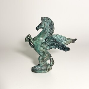 May include: A green bronze sculpture of a winged horse, or Pegasus, with its wings spread out. The sculpture is standing on a base.
