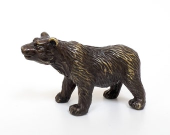 May include: A small bronze sculpture of a bear standing on all fours. The bear is facing to the right and has a detailed, textured fur.