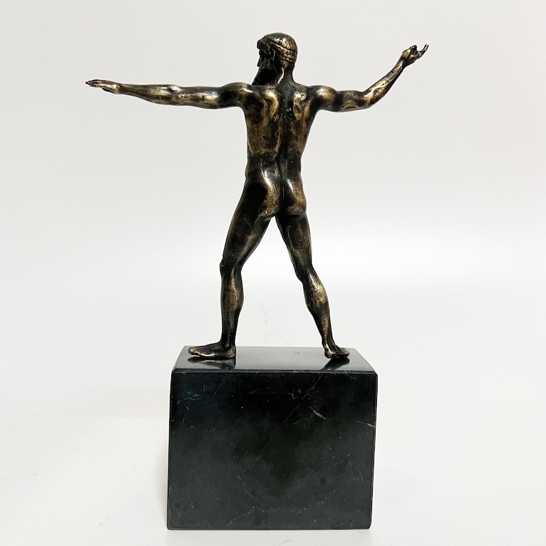 May include: Bronze sculpture of a nude male figure standing with arms outstretched. The sculpture is on a black marble base.