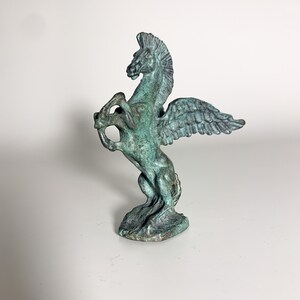 May include: A green bronze statue of a winged horse, or Pegasus, with its wings spread out. The horse is standing on its hind legs and has a proud expression on its face.