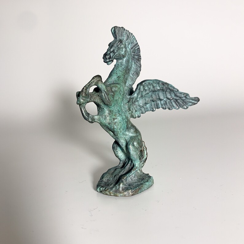 May include: A green bronze statue of a winged horse, or Pegasus, with its wings spread out. The horse is standing on its hind legs and has a proud expression on its face.