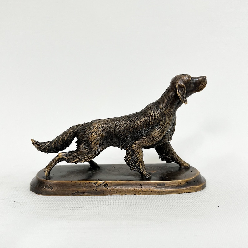 May include: A bronze sculpture of a dog running, set on a rectangular base. The dog is brown and black and has its head turned to the side.