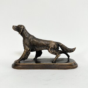 May include: A bronze sculpture of a brown and black Irish Setter dog standing on a rectangular base. The dog is in a running pose with its head turned to the side.