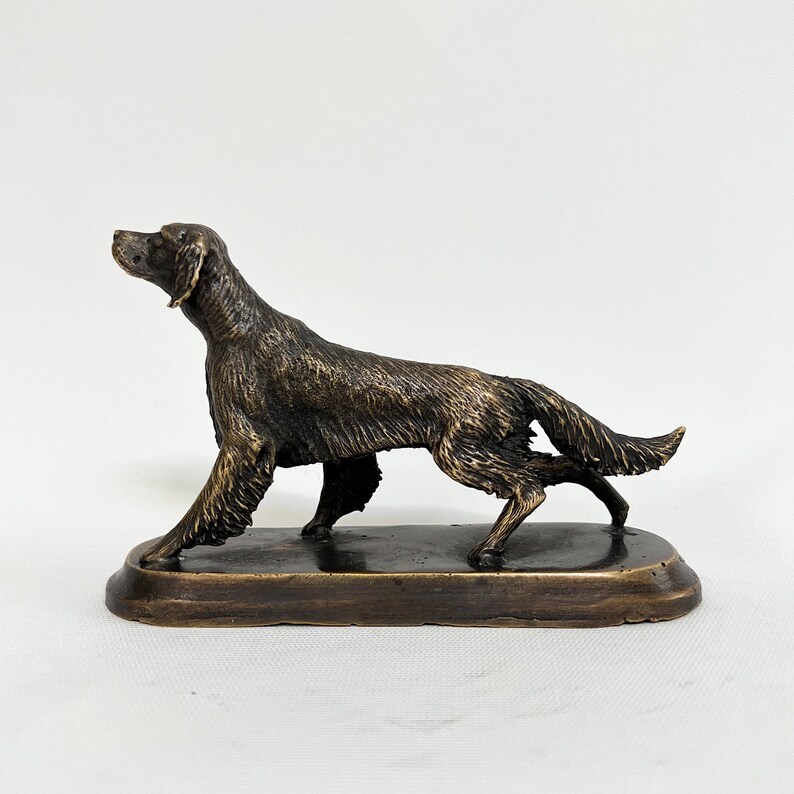May include: A bronze sculpture of a brown and black Irish Setter dog standing on a rectangular base. The dog is in a running pose with its head turned to the side.