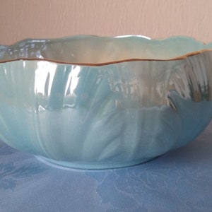 May include: A pale blue ceramic bowl with a wavy edge and a gold trim. The bowl features a textured, ridged pattern on the outside. The inside has a pearlescent finish. This decorative bowl is suitable for serving or display.