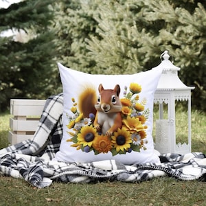 May include: White throw pillow with a cute cartoon squirrel surrounded by sunflowers and other flowers. The squirrel is brown and has a white belly. The pillow is on a black and white plaid blanket.