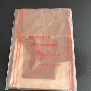 May include: A pair of tan-colored nylon stockings packaged in a clear plastic sleeve. The packaging features red text that reads Seamfree, Micro Mesh, Nylons, and MADE IN ENGLAND, with two vertical red lines running down the sides of the plastic.