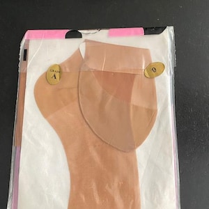 May include: A pair of sheer beige stockings packaged in a clear plastic sleeve. The stockings feature a reinforced heel and toe area. Two gold oval stickers are attached to the front, one labeled Grade A and the other displaying the number 9.