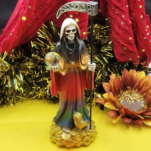 May include: A multi-colored figurine of Santa Muerte, the Mexican folk saint of death, holding a crystal ball and a scythe. The figurine is standing on a base of gold coins.