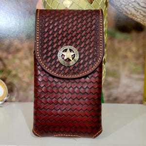 May include: A brown leather phone case with a woven pattern and a star-shaped metal accent. The case has a flap that closes with a snap.