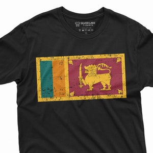 Może przedstawiać: Czarny T-shirt z nadrukiem vintage flagi Sri Lanki na przodzie. Flaga przedstawia lwa trzymającego miecz, otoczonego czterema liśćmi. Flaga jest w odcieniach zieleni, pomarańczy, żółci i czerwieni.