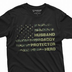 May include: Black t-shirt with a distressed American flag design. The flag is made up of camouflage print and has the words "Husband, Daddy, Protector, Hero" written on it.