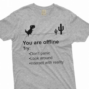 May include: A gray t-shirt with a black pixelated dinosaur and cacti graphic. The text "You are offline" is printed on the shirt, followed by "Try:" and a list of three bullet points: "Don't panic", "Look around", and "Interact with reality".