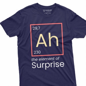 Pode incluir: Uma camiseta azul marinho com um gráfico branco de um elemento da tabela periódica. O elemento é rotulado como "Ah" com o número atômico 29,7 e o peso atômico 230. O texto "the element of Surprise" está abaixo do gráfico do elemento.