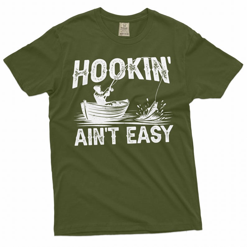 K&ouml;nnte beinhalten: Ein gr&uuml;nes T-Shirt mit einer wei&szlig;en Grafik einer Person, die von einem Boot aus angelt. Der Text auf dem Shirt lautet "Hookin' Ain't Easy".