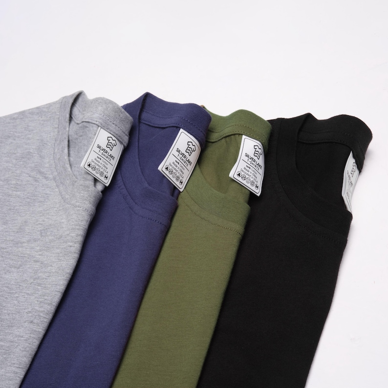 May include: Four t-shirts in different colors: gray, blue, green, and black. Each shirt has a white tag with the text "Silver Lake Apparel" and care instructions.