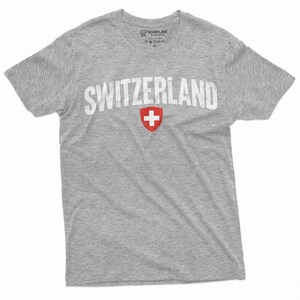 May include: A grey t-shirt with a white distressed graphic of the word "SWITZERLAND" and the Swiss flag.