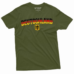 May include: A green t-shirt with the word "DEUTSCHLAND" printed in black, red, and yellow letters. The German flag colors are incorporated into the letters. A yellow and black German eagle is printed below the word.