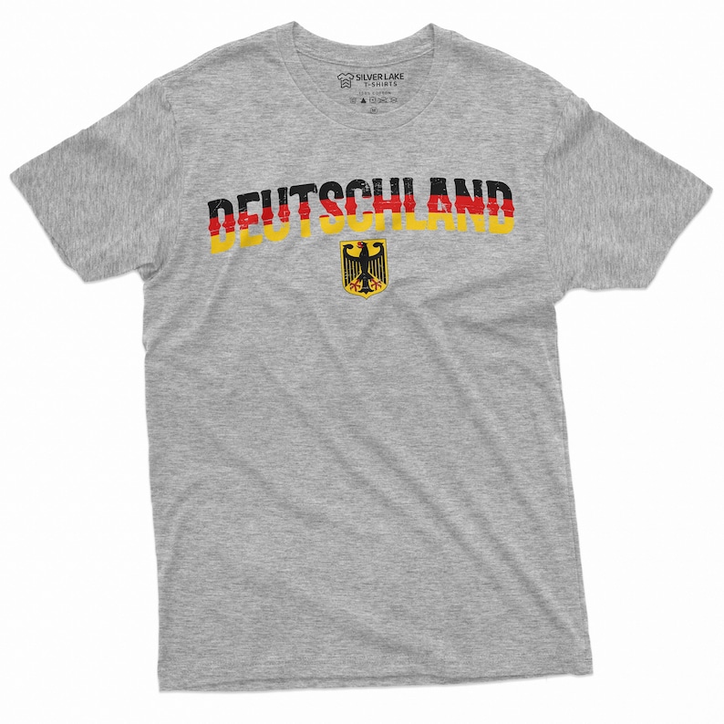 May include: A gray t-shirt with the word "DEUTSCHLAND" printed in red, yellow, and black, with the German flag colors. The German coat of arms is printed below the word.
