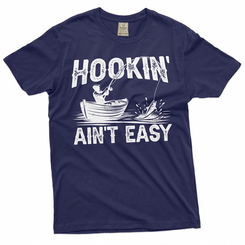 K&ouml;nnte beinhalten: Ein marineblaues T-Shirt mit einer wei&szlig;en Grafik einer Person, die von einem Boot aus angelt. Der Text "HOOKIN' AINT EASY" ist in Wei&szlig; auf das Shirt gedruckt.