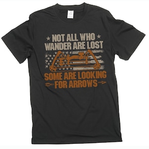May include: Black t-shirt with the text "NOT ALL WHO WANDER ARE LOST, SOME ARE LOOKING FOR ARROWS." The design includes a bow and arrow graphic with a faded American flag background. The shirt is made of a soft material.