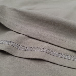 Puede incluir: Primer plano de una tela gris con una costura cosida. La tela est&aacute; doblada, mostrando el rev&eacute;s de la tela.