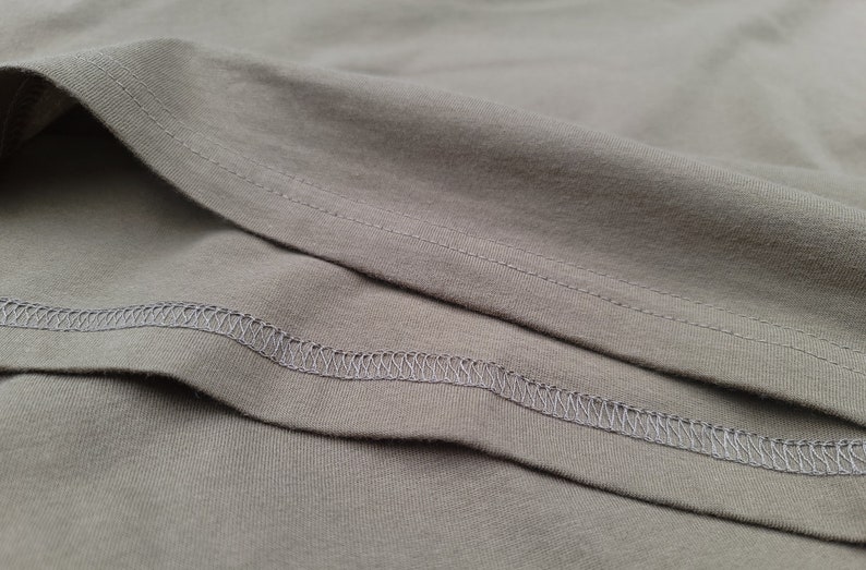 Puede incluir: Primer plano de una tela gris con una costura cosida. La tela est&aacute; doblada, mostrando el rev&eacute;s de la tela.