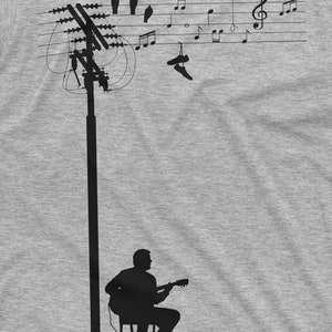 K&ouml;nnte beinhalten: Eine Silhouette einer Person, die Gitarre spielt unter einer Stromleitung mit einem Ballon, Schuhen und V&ouml;geln, die daran h&auml;ngen. Musiknoten sind auf die Stromleitungen gezeichnet.
