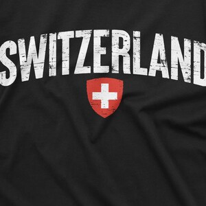 May include: Black t-shirt with white distressed text that reads "SWITZERLAND" and a red Swiss flag with a white cross in the centre.
