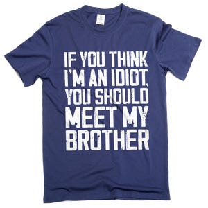 May include: Navy blue t-shirt with white text that reads: "IF YOU THINK I'M AN IDIOT, YOU SHOULD MEET MY BROTHER." The shirt has a crew neck and short sleeves. The text is in a bold, sans-serif font.