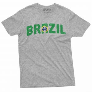 Puede incluir: Una camiseta gris con un gr&aacute;fico verde y amarillo desgastado de la palabra "BRAZIL" con la bandera brasile&ntilde;a en el medio de la palabra.
