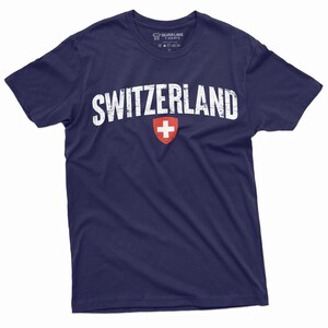 May include: A navy blue t-shirt with a white distressed graphic of the word "SWITZERLAND" and the Swiss flag.