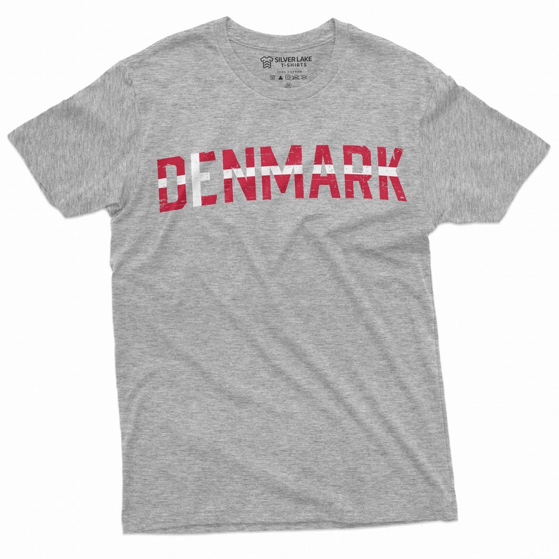 May include: A gray t-shirt with the word "DENMARK" printed in red and white letters. The letters are stylized to look like the Danish flag.