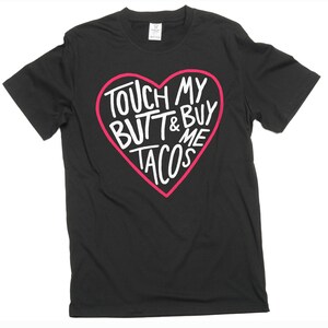 Pode incluir: Camiseta preta com um desenho em forma de coração rosa. O coração contém o texto branco "TOUCH MY BUTT & BUY ME TACOS". A camiseta tem mangas curtas e gola redonda.