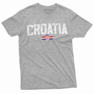 以下が含まれることがあります： グレーのTシャツに、くたびれた感じの白い文字で「CROATIA」とプリントされています。その下にクロアチアの旗がプリントされています。