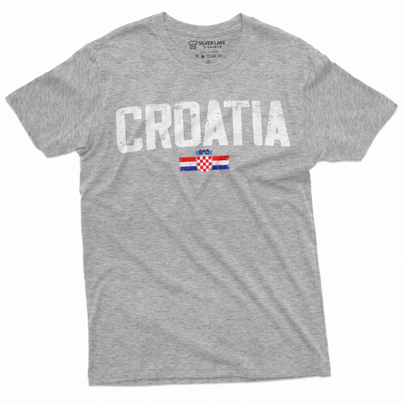 以下が含まれることがあります： グレーのTシャツに、くたびれた感じの白い文字で「CROATIA」とプリントされています。その下にクロアチアの旗がプリントされています。
