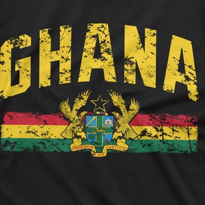 May include: A black t-shirt with a yellow distressed graphic of the word "GHANA" and a red, yellow, green, and black flag with a coat of arms featuring a star, eagle, and the words "Freedom and Justice".